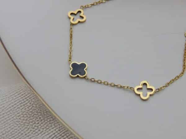 Close-up of four-leaf clover charm bracelet in gold and black enamel – Royal Reflection Dazzling Studio.
