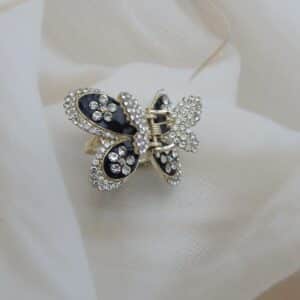 Large butterfly-shaped hair claw clip in a gold tone with black enamel and clear sparkling rhinestone studs, elegant hair accessory.