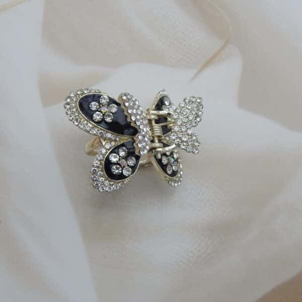 Large butterfly-shaped hair claw clip in a gold tone with black enamel and clear sparkling rhinestone studs, elegant hair accessory.