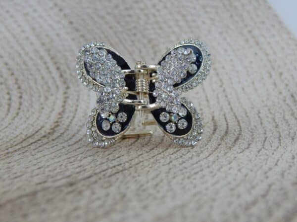 Large butterfly-shaped hair claw clip in a gold tone with black enamel and clear sparkling rhinestone studs, elegant hair accessory.