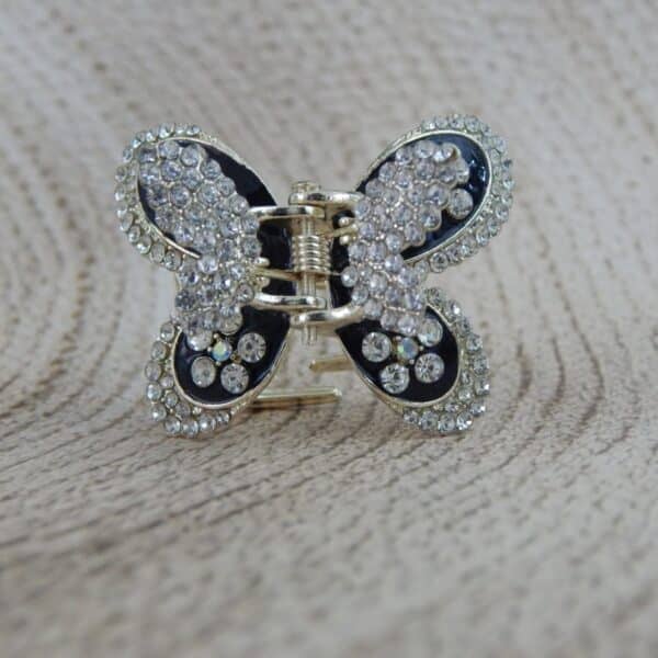 Large butterfly-shaped hair claw clip in a gold tone with black enamel and clear sparkling rhinestone studs, elegant hair accessory.