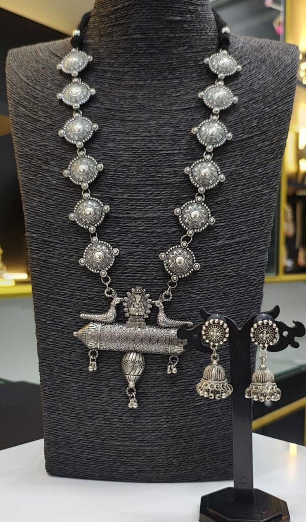 Oxidised long necklace set with round motifs and peacock pendant paired with jhumka earrings on display stand