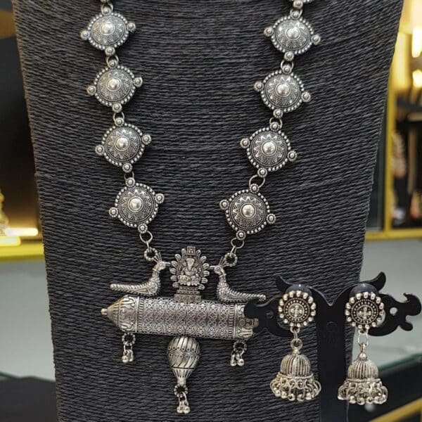 Oxidised long necklace set with round motifs and peacock pendant paired with jhumka earrings on display stand
