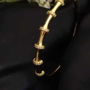 angled view of Bamboo anti tarnish kada for women in gold-toned segmented design with American diamond stones