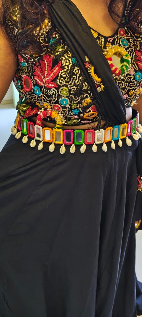 Multicolour mirror work waist belt with cowrie-style drops worn over a black outfit for garba