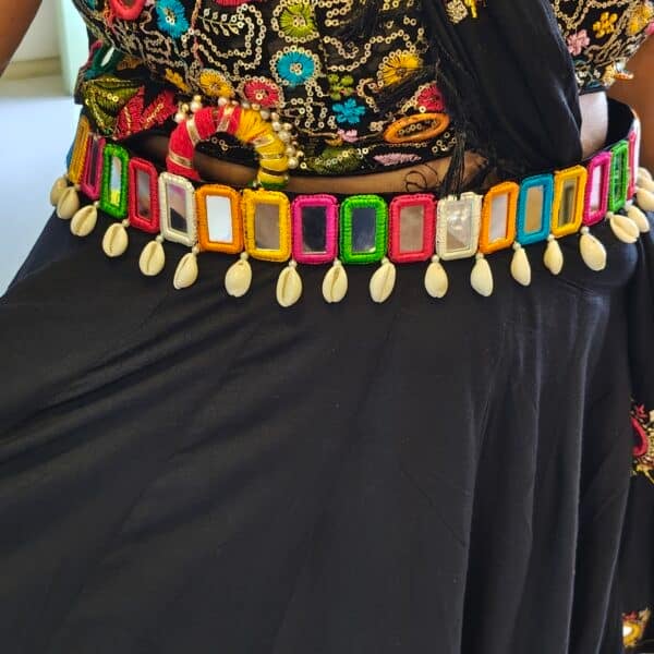Multicolour mirror work waist belt with cowrie-style drops worn over a black outfit for garba
