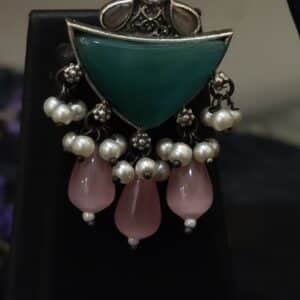 Detail of oxidised earring with green stone shield and pink stone drops