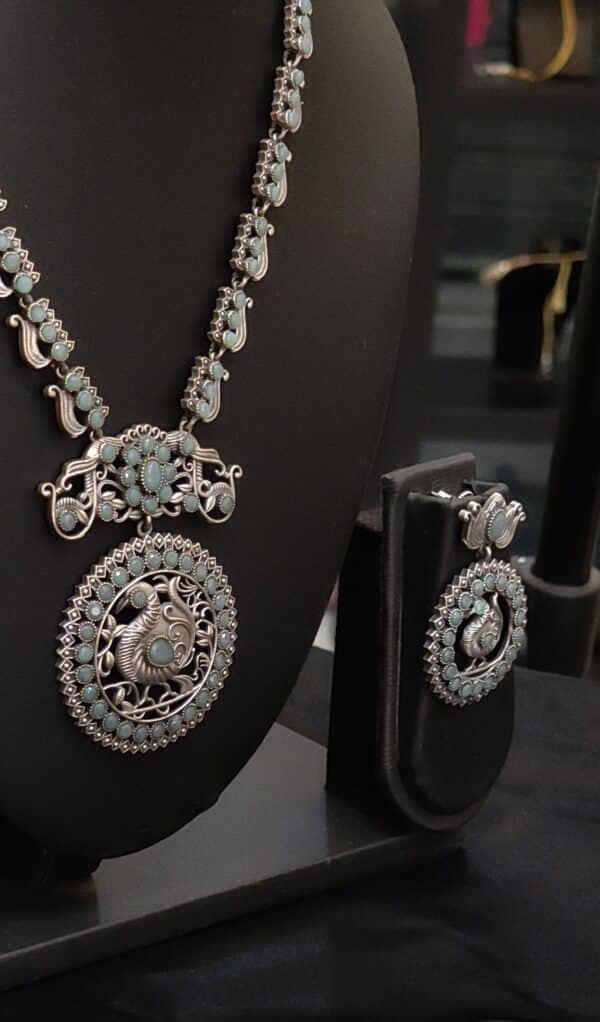 Close-up of peacock medallion pendant in oxidised brass with sea green stones