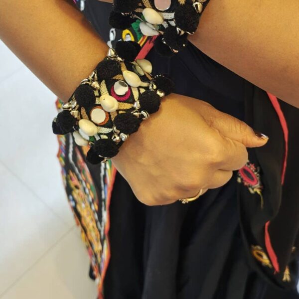 Black pom pom cuff bracelet with mirror discs and cowrie-style details worn on both wrists for garba