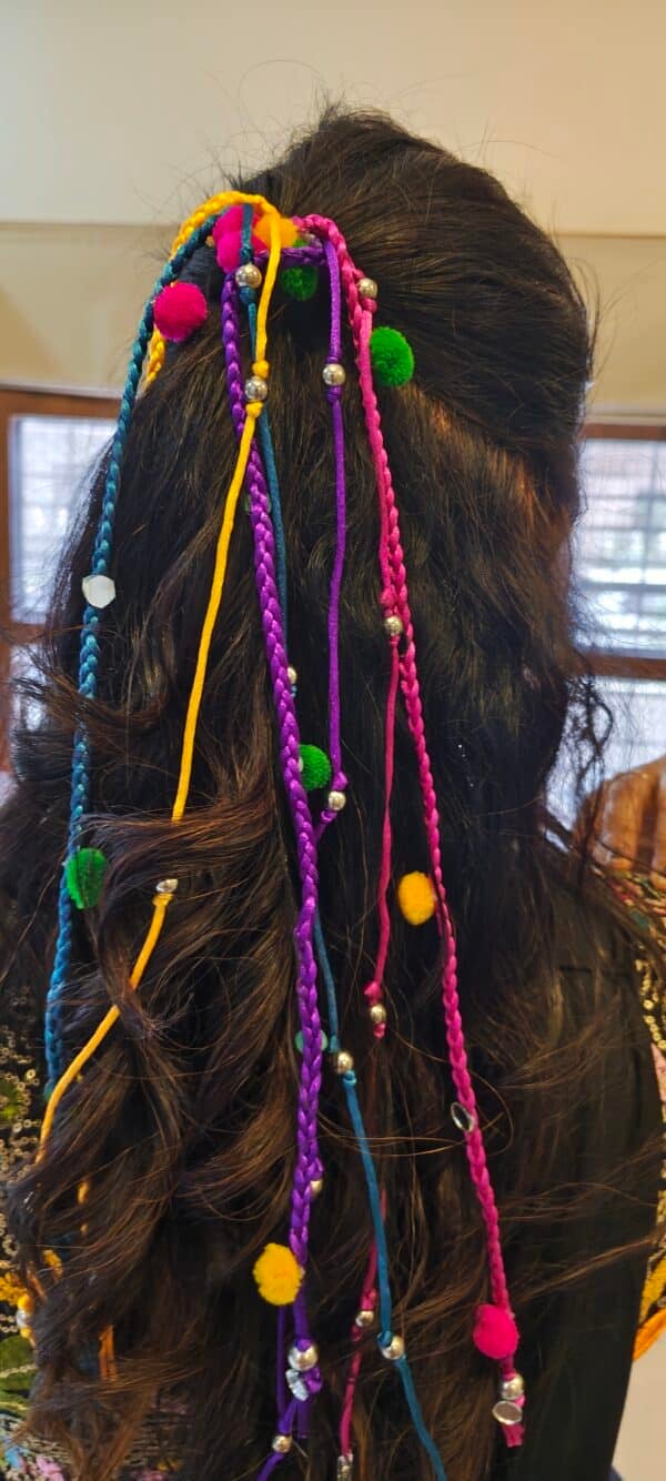 Multicolour pom pom hair tassel with braided cords and silver-finish beads worn in a ponytail for garba