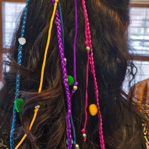 Multicolour pom pom hair tassel with braided cords and silver-finish beads worn in a ponytail for garba